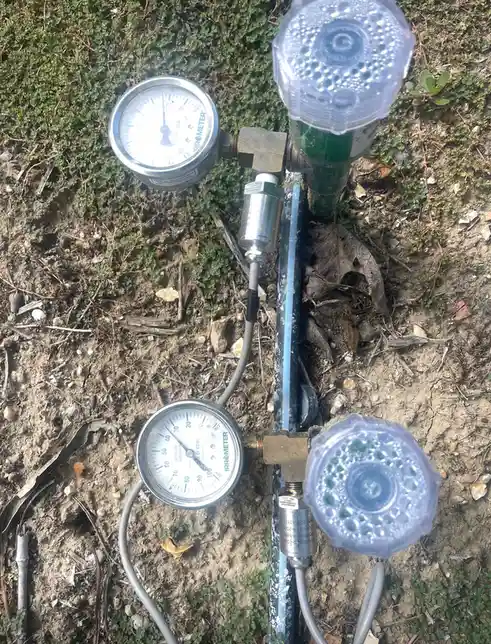 An outdoor photo shows two irrigation system pressure gauges mounted on a metal pipe, with clear plastic caps on the…