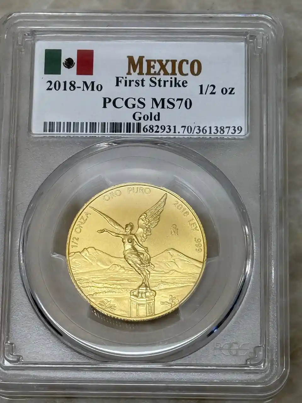 A professionally graded 2018-Mexico 1/2 oz gold coin, featuring the Winged Victory design, is encased in a PCGS MS70 holder…