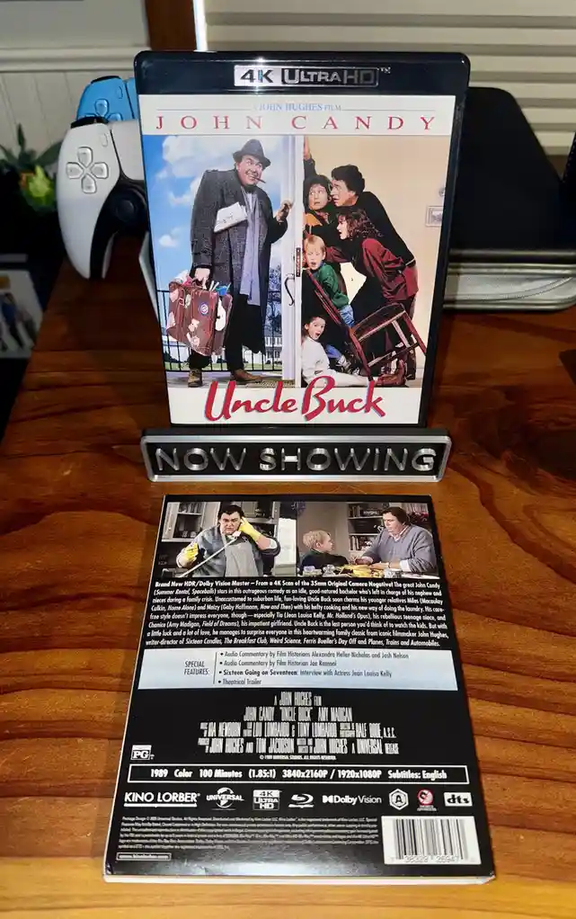 A 4K Ultra HD Blu-ray case for the 1989 film 'Uncle Buck' starring John Candy is displayed upright on a wooden table, with…
