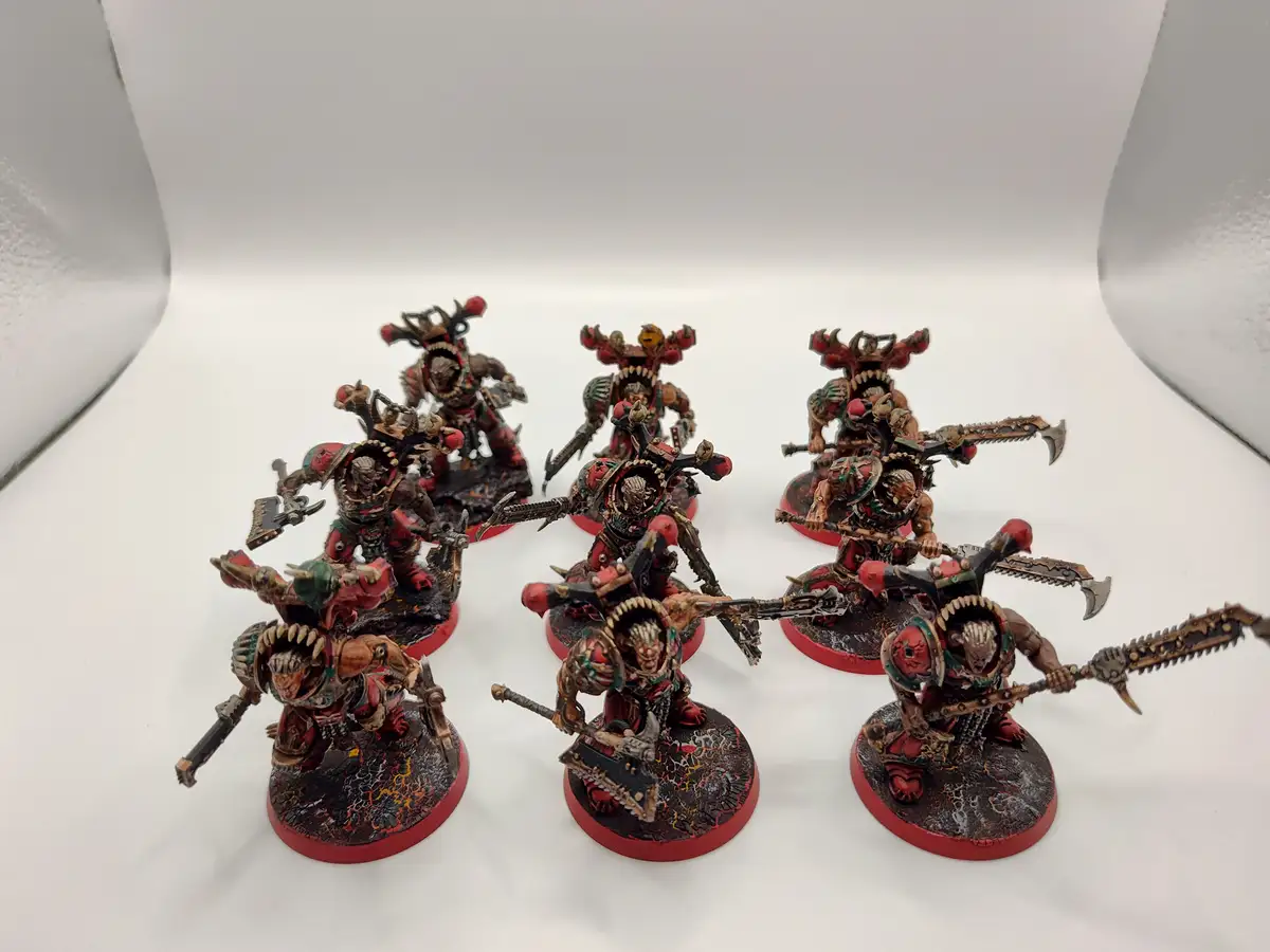Seven hand-painted Warhammer 40,000 miniatures, likely Chaos Space Marines or similar, are arranged on a white surface. They…