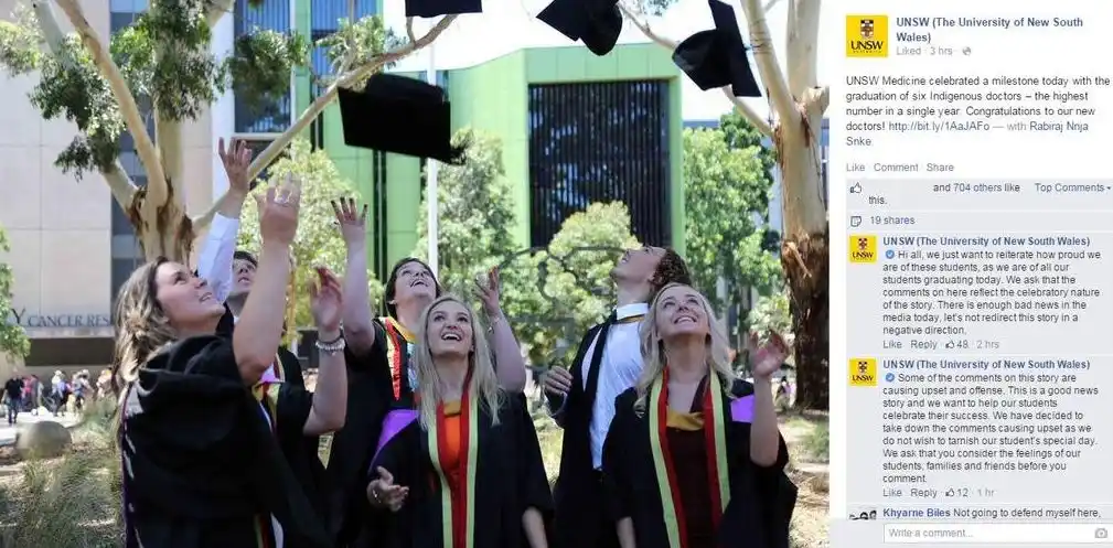 A group of graduates in black caps and gowns joyfully toss their graduation caps into the air outdoors. The image is a…