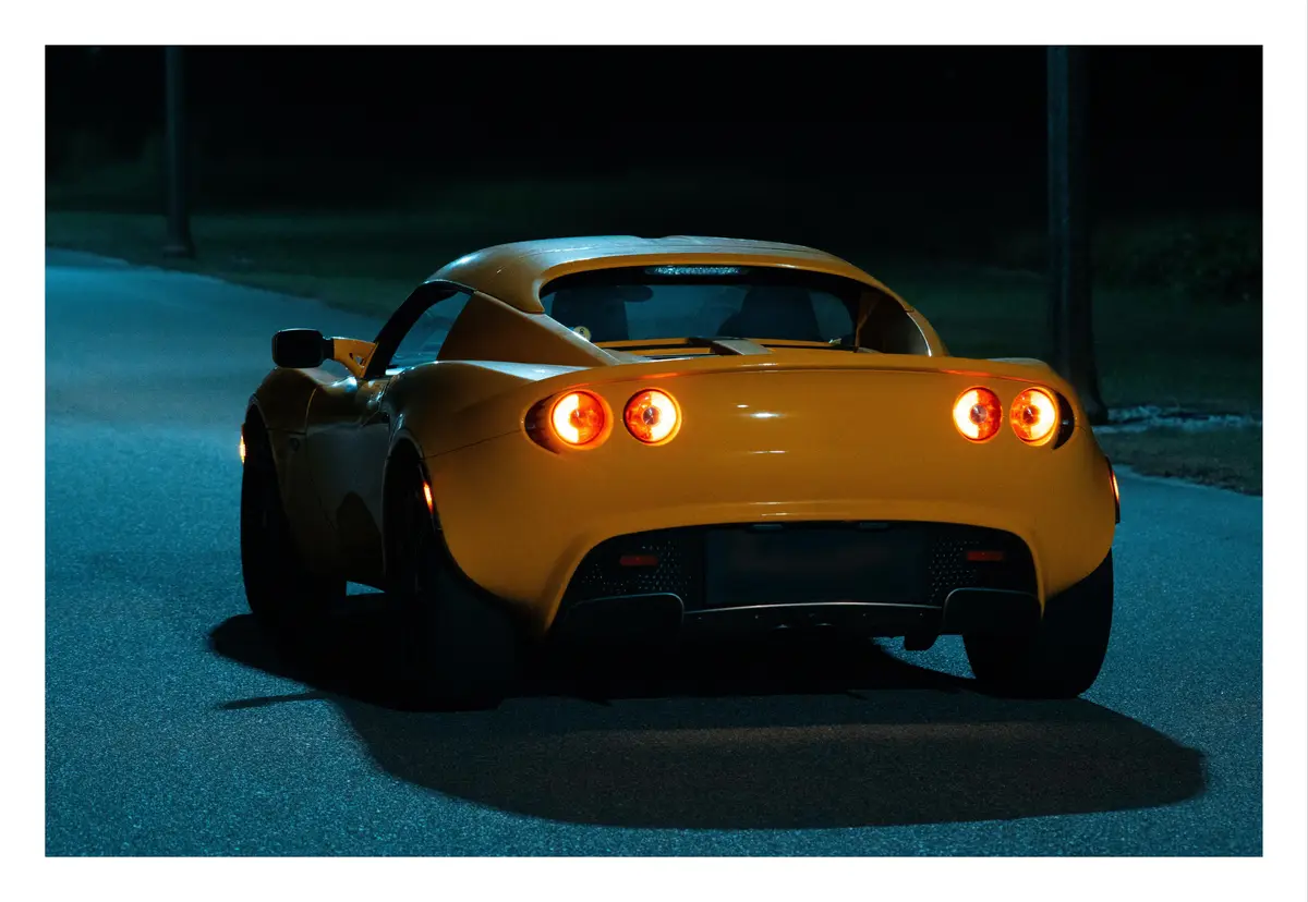 A yellow sports car is parked at night on a street, its rear lights glowing orange. The car's sleek design and the dark…