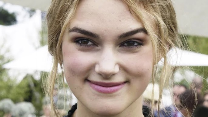 A close-up photo of a young woman with blonde hair and a subtle smile, looking directly at the camera. The overlaid text…