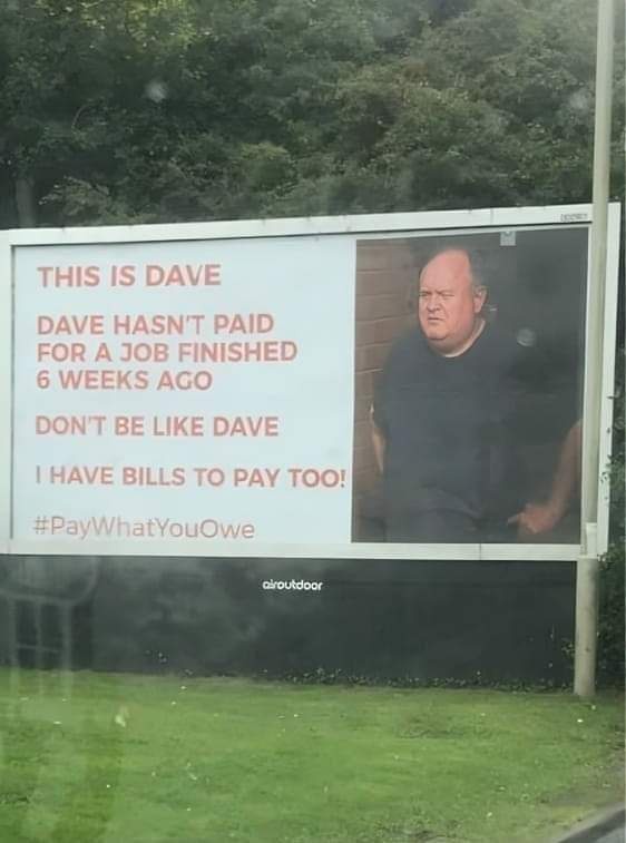 A large outdoor billboard features a photo of a man with a stern expression next to red text detailing a fictional person…
