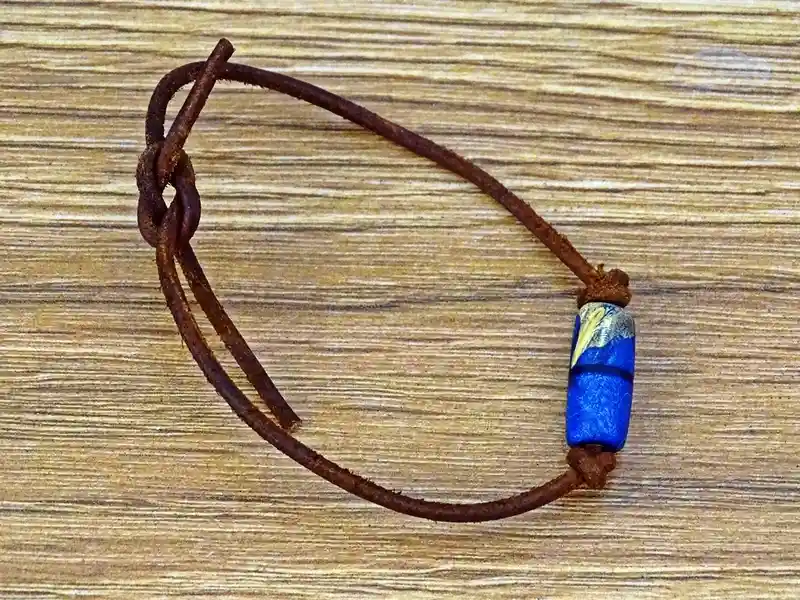 A simple brown leather bracelet with a single blue and gold bead rests on a wooden surface. The overlaid text reads 'i'm not…