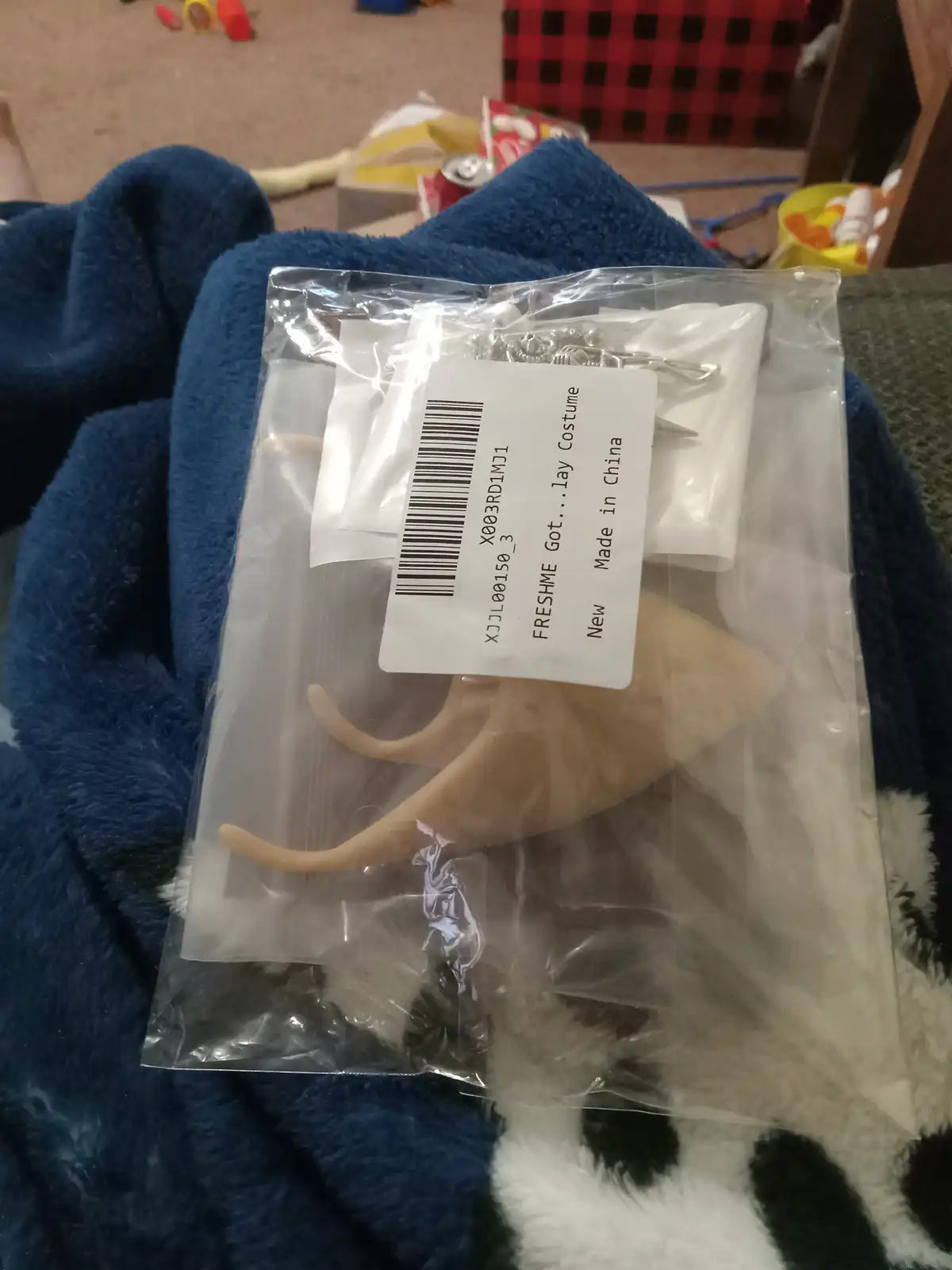 A clear plastic bag containing a costume prop with three curved, beige plastic claws and some metal hooks, sits on a blue…