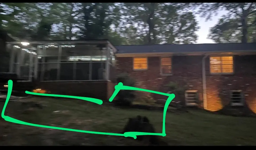 a blurry nighttime photo of a brick house with lit windows and a screened porch, with a bright green hand-drawn rectangle…