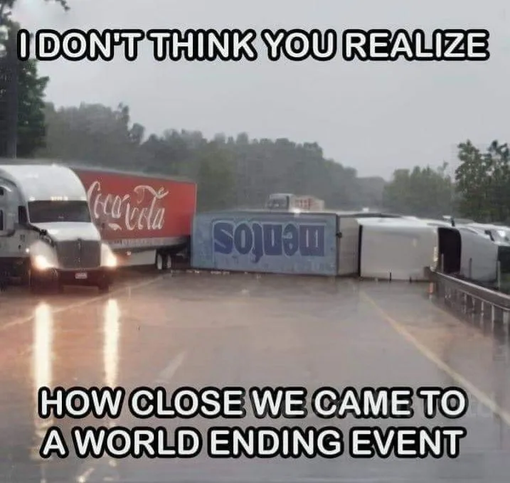 A rainy highway scene shows a Coca-Cola branded semi-truck driving past a severely damaged, overturned Mentos truck. The…