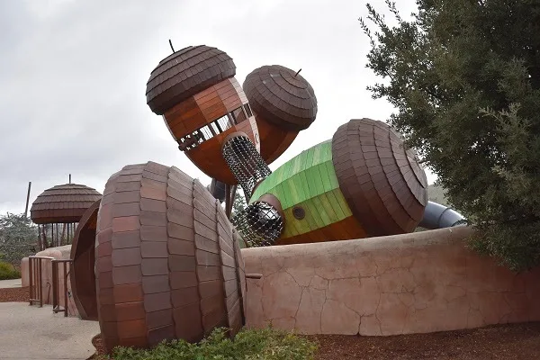 A large, whimsical sculpture of oversized acorns and a green-striped caterpillar-like creature, all made of wooden shingles…