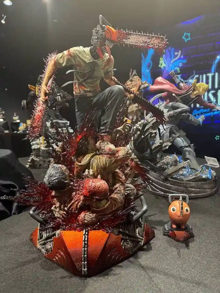 A highly detailed, gory statue of the anime character Chainsaw Man, depicted mid-action with a chainsaw for a head, standing…