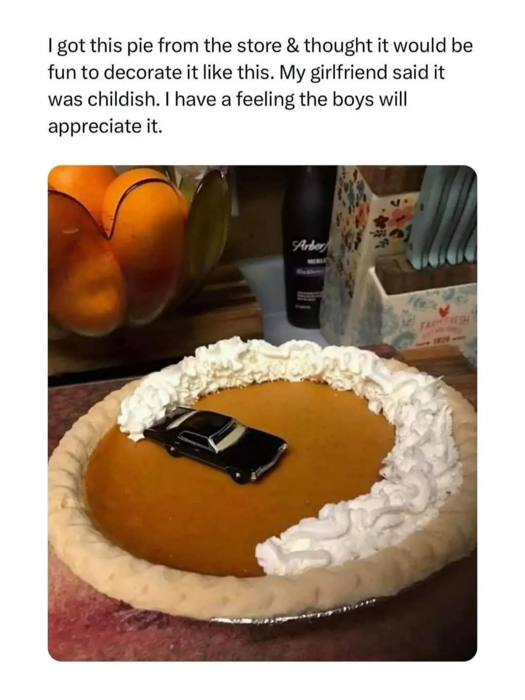 A pumpkin pie with whipped cream piped along the edge and a small black toy car placed in the center. The overlaid text…