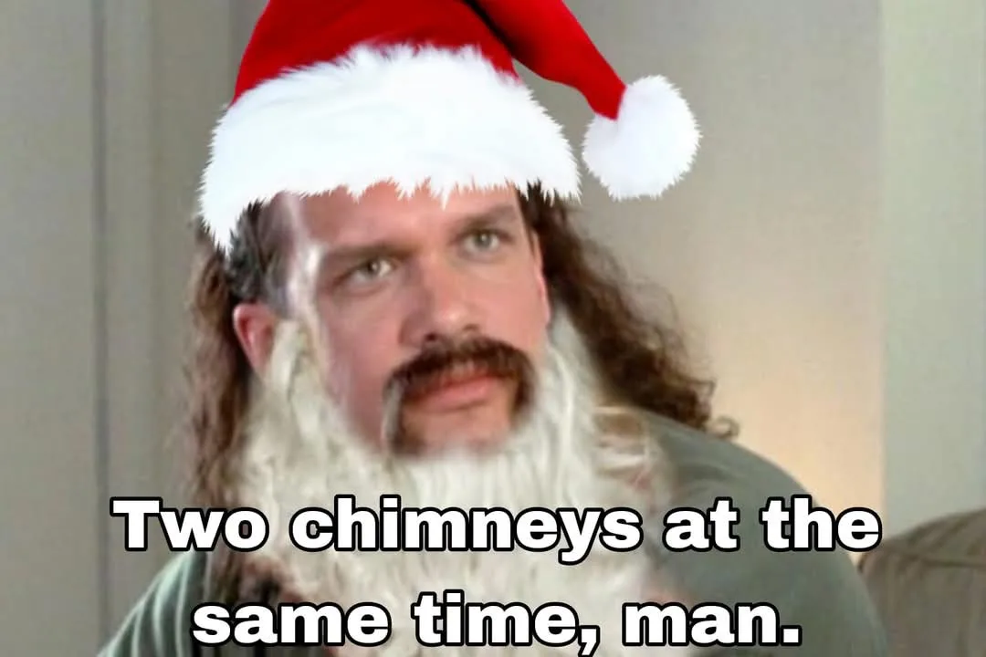 A man with long hair, a mustache, and a white beard wears a red and white Santa hat. He stares intently forward with a…