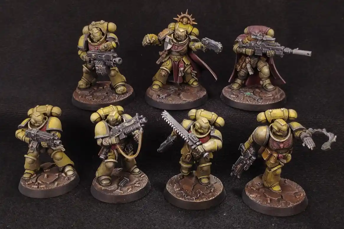 Seven painted miniature figurines of Space Marines in yellow armor, each holding different weapons and posed on rocky bases…