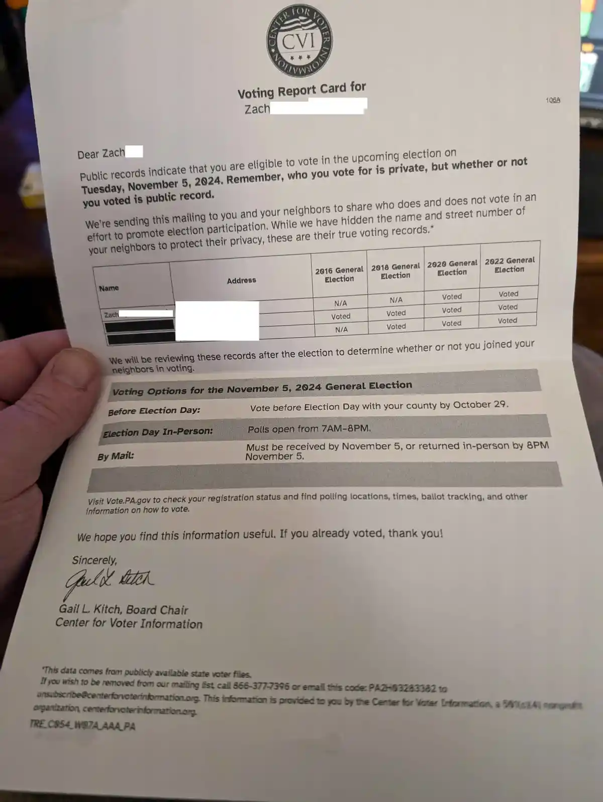 A person holds a 'Voting Report Card' from the Center for Voter Information, addressed to 'Zach'. The document states that…