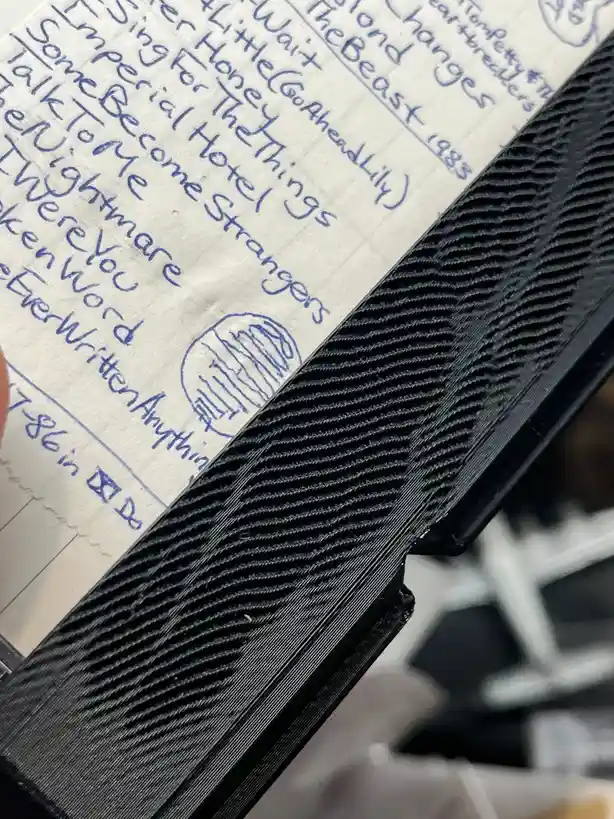 A close-up photo shows a handwritten list of song titles and artist names in blue ink on lined paper, partially obscured by…