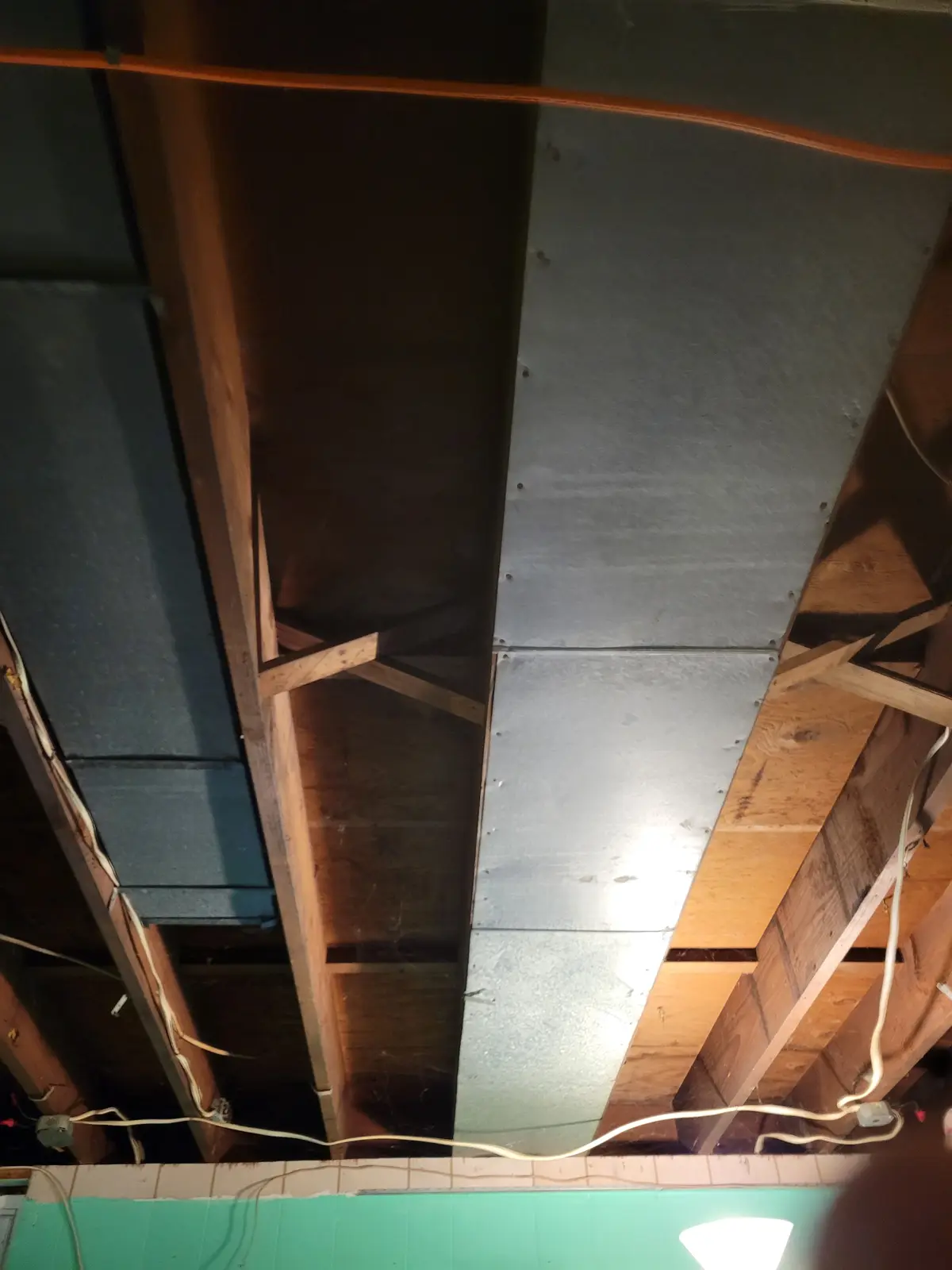 A low-angle photo shows an unfinished ceiling with exposed wooden beams, metal panels, and dangling wires. The overlaid text…