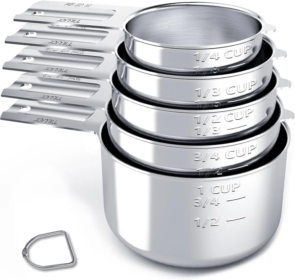 A set of five nested stainless steel measuring cups, stacked from smallest to largest, with engraved volume markings like…