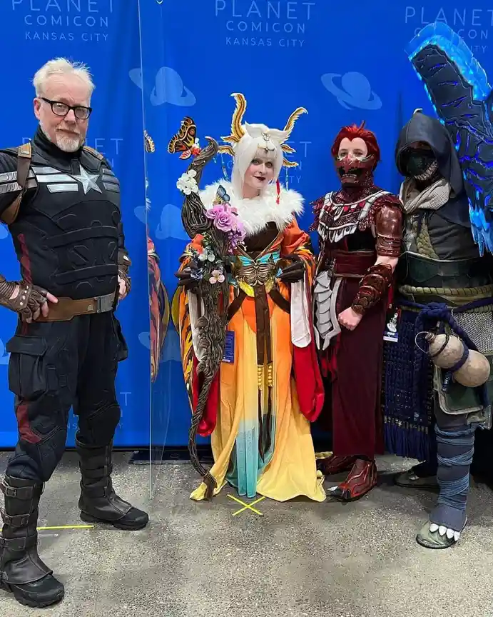Four people in elaborate cosplay stand in front of a blue 'Planet Comicon Kansas City' backdrop. From left to right: a man…