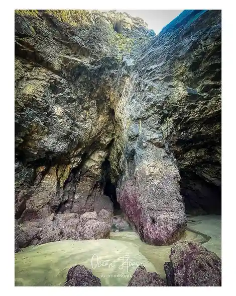 A scenic photo of a narrow rocky cove with clear shallow water and textured cliffs, featuring a watermark in the bottom…