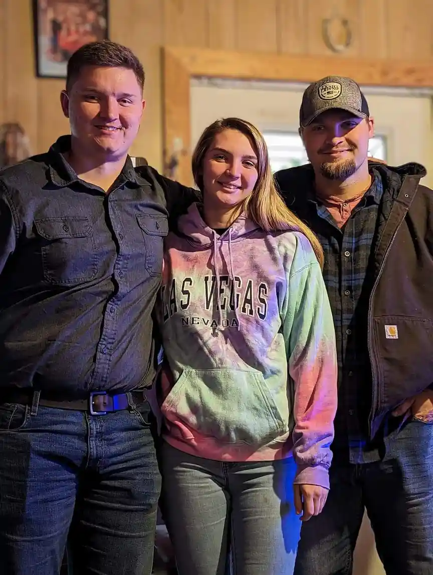 Three people pose for a photo indoors; the person in the center wears a tie-dye hoodie with 'LAS VEGAS NEVADA' printed on…