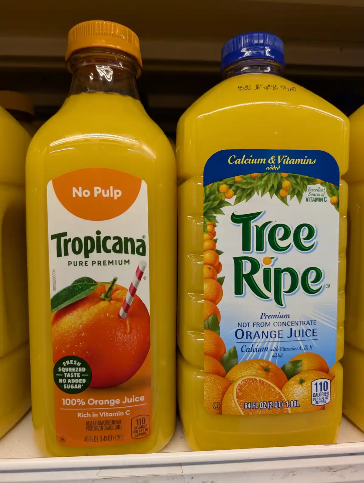Two large bottles of orange juice sit side-by-side on a store shelf: a Tropicana Pure Premium bottle with a yellow cap and…