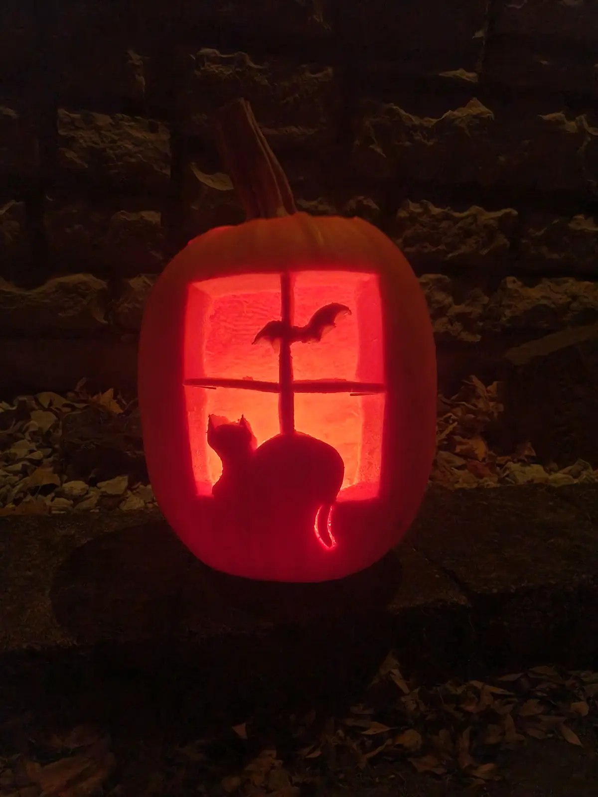 A carved Halloween pumpkin with a glowing red interior, featuring a window design with a cat silhouette looking out and a…
