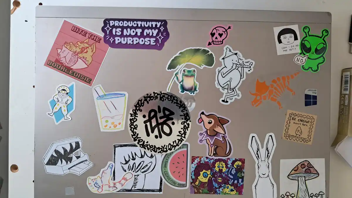 A beige fridge door covered in various colorful stickers, including a prominent purple one that reads 'PRODUCTIVITY IS NOT…