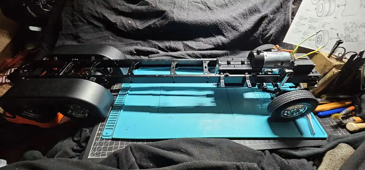 A partially assembled RC car chassis sits on a blue plastic mat labeled 'Circuit board location area', surrounded by tools…