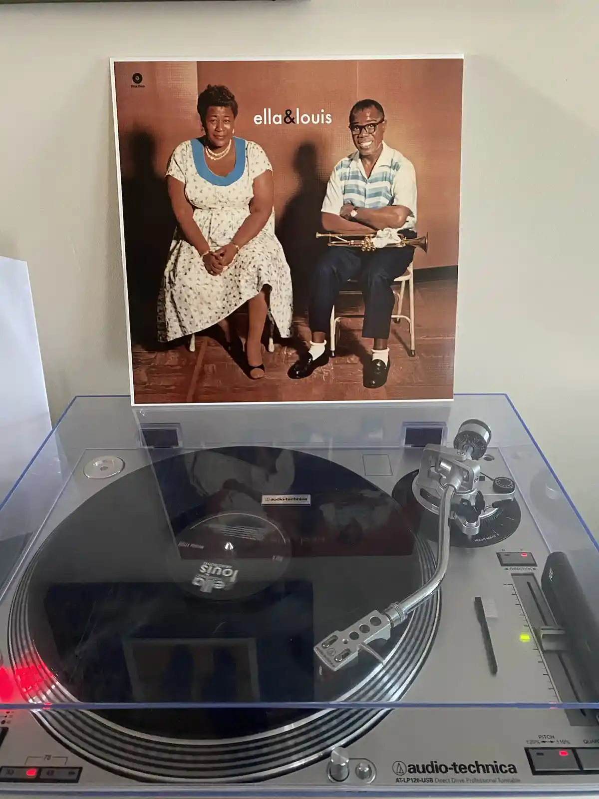 A vinyl record sleeve featuring Ella Fitzgerald and Louis Armstrong sitting together, placed upright on a modern…
