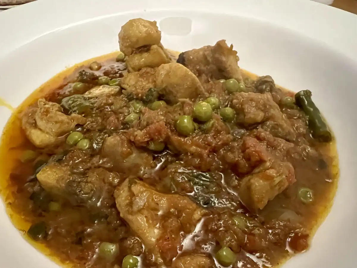 A close-up photo shows a white bowl filled with a thick, orange-brown stew containing chunks of what appears to be fried…