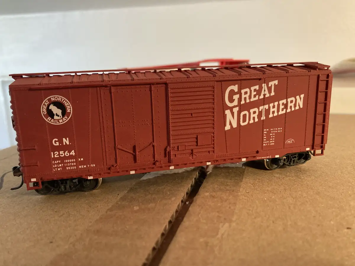 A red model train boxcar with 'GREAT NORTHERN' written in large white letters on its side, featuring a circular logo with a…