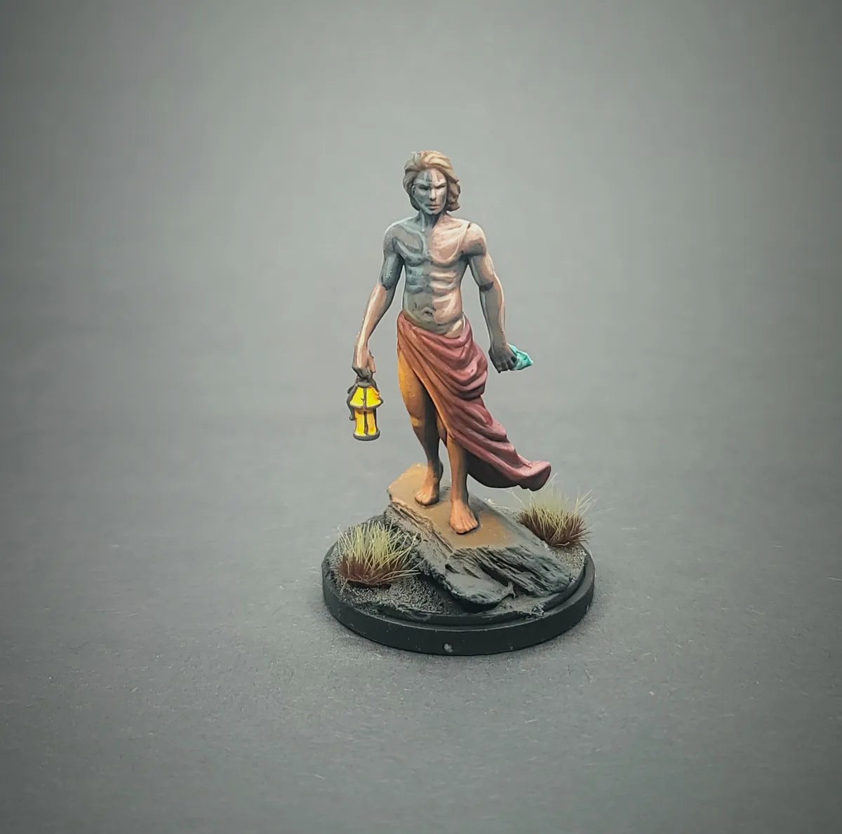 A painted tabletop miniature of a muscular, shirtless humanoid figure with half his body painted gray and the other half…