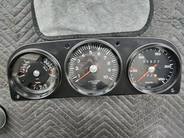 A close-up photo of a vintage car's dashboard with three gauges: fuel, tachometer, and speedometer. The speedometer needle…