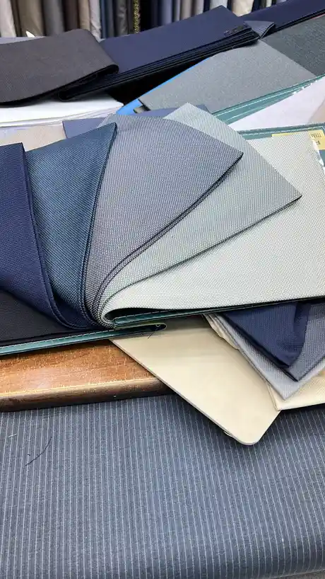 A close-up shot of a pile of folded fabric swatches in various shades of blue, gray, and beige, displayed on a wooden…