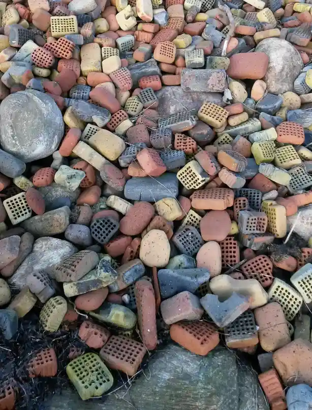 A pile of weathered, colorful bricks and smooth river rocks mixed together, with some bricks showing their characteristic…
