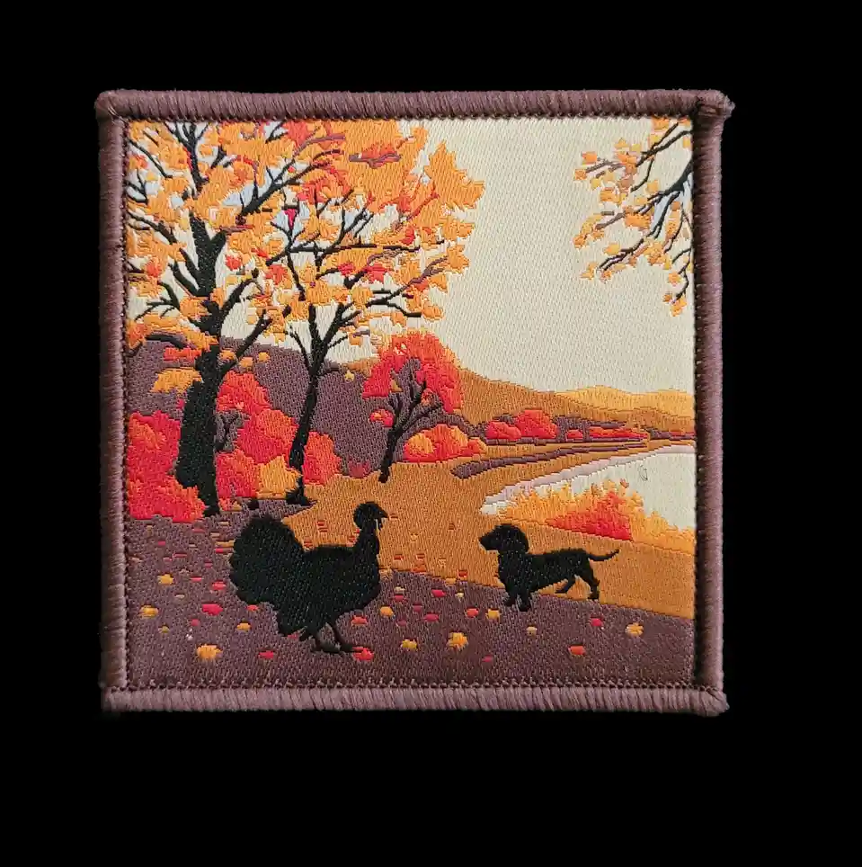 An embroidered patch depicts a stylized autumn scene with trees in orange and red foliage, a body of water, and scattered…