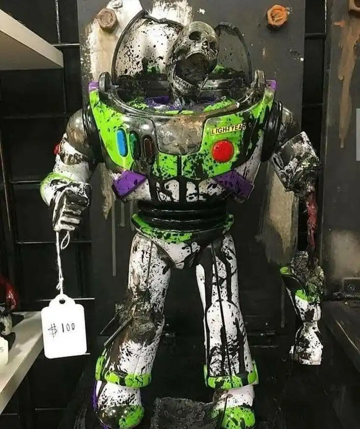 A heavily damaged, melted, and splattered Buzz Lightyear action figure stands in a dark room, its head a skull-like mess…