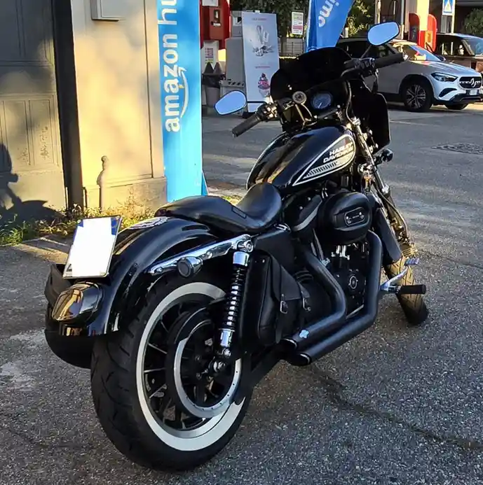 A black Harley-Davidson motorcycle is parked on a paved surface next to a blue Amazon banner. The bike has chrome accents, a…