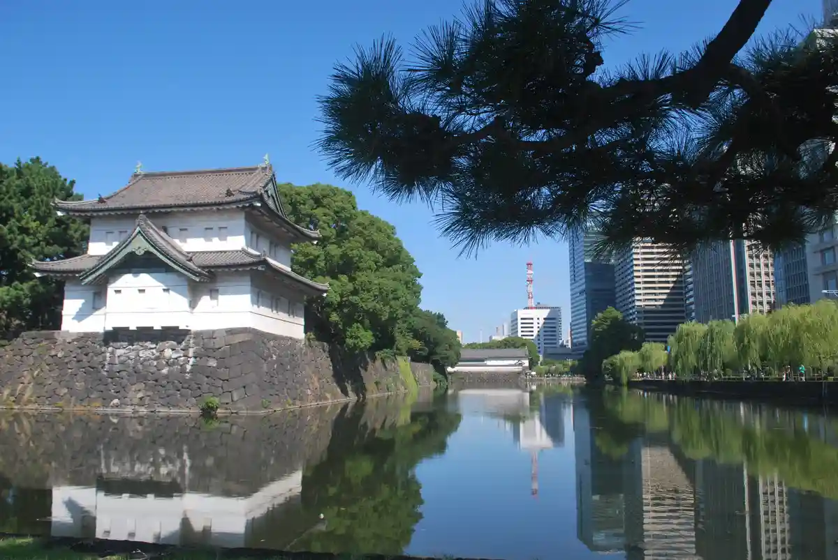 A serene photo of the Tokyo Imperial Palace's traditional white and grey castle structure with a stone wall, reflected in a…