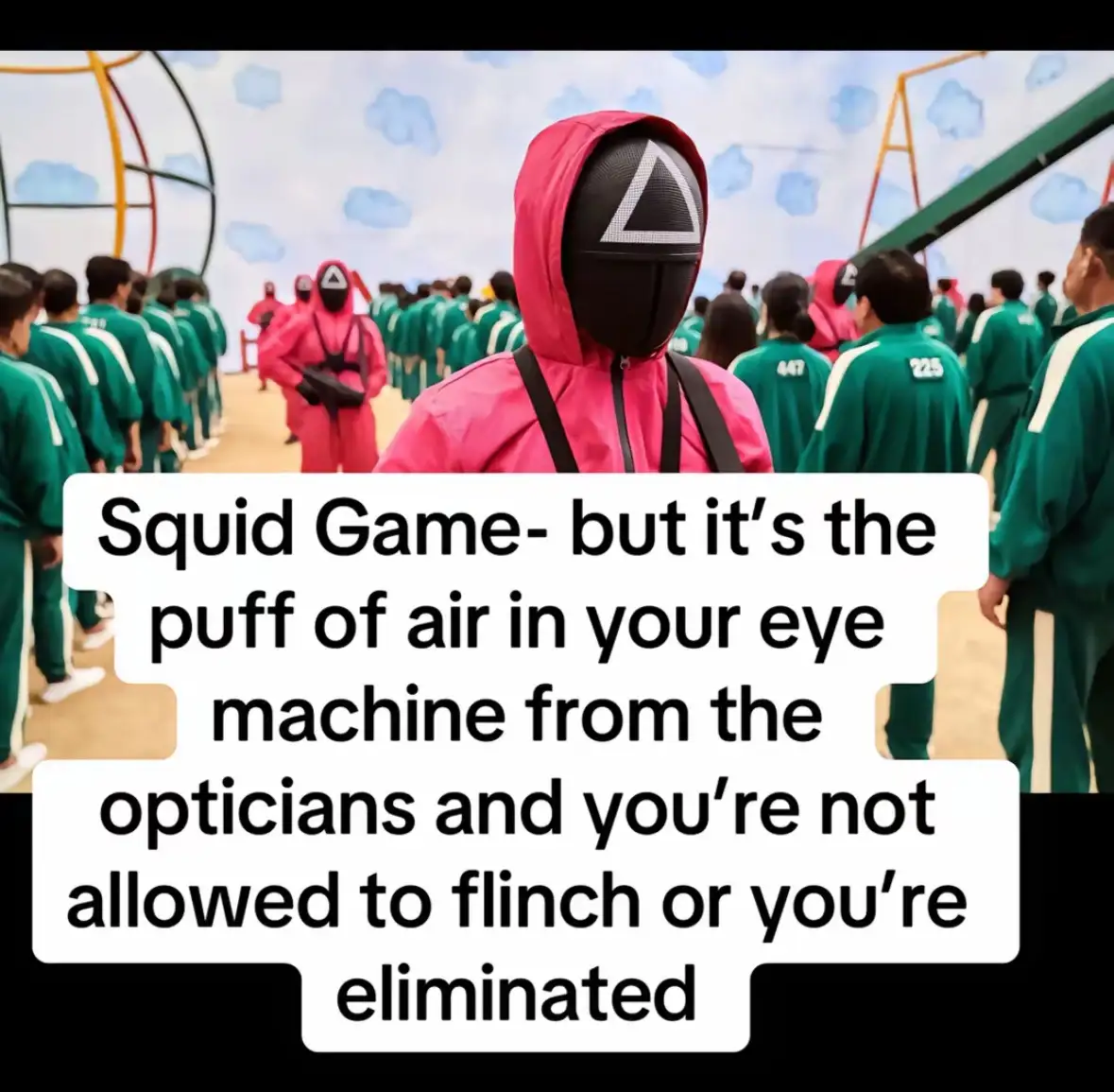 A still from the show 'Squid Game' featuring a player in a pink hoodie and black mask with a white triangle, standing in…