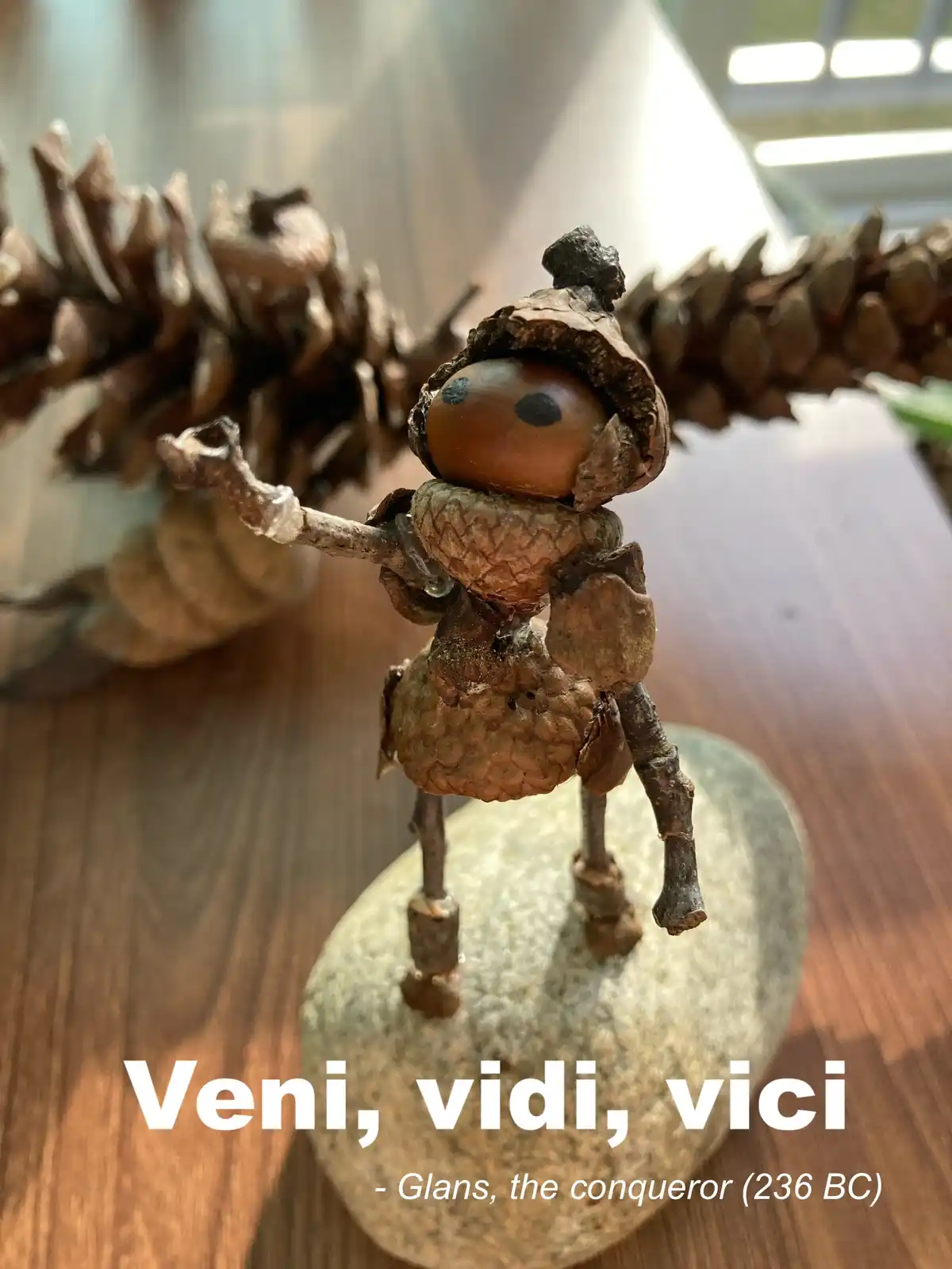 A small figurine crafted from natural materials like acorns, pinecones, and twigs stands on a stone base, posed as if…