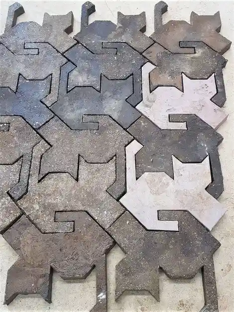 The image shows a pile of irregularly shaped, weathered concrete pavers, each cut into the silhouette of a cat, arranged…