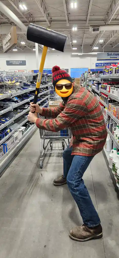 A person in a plaid shirt and a red 'ho ho ho' beanie, with a smiling emoji covering their face, is posing in a hardware…