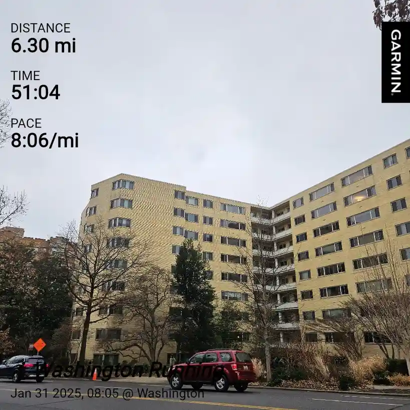 A Garmin fitness tracker screenshot overlaying a photo of a large, beige apartment building on a cloudy day. The text shows…