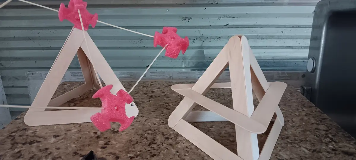 Two handmade catapults constructed from popsicle sticks sit on a speckled countertop, aimed at each other. Each catapult has…