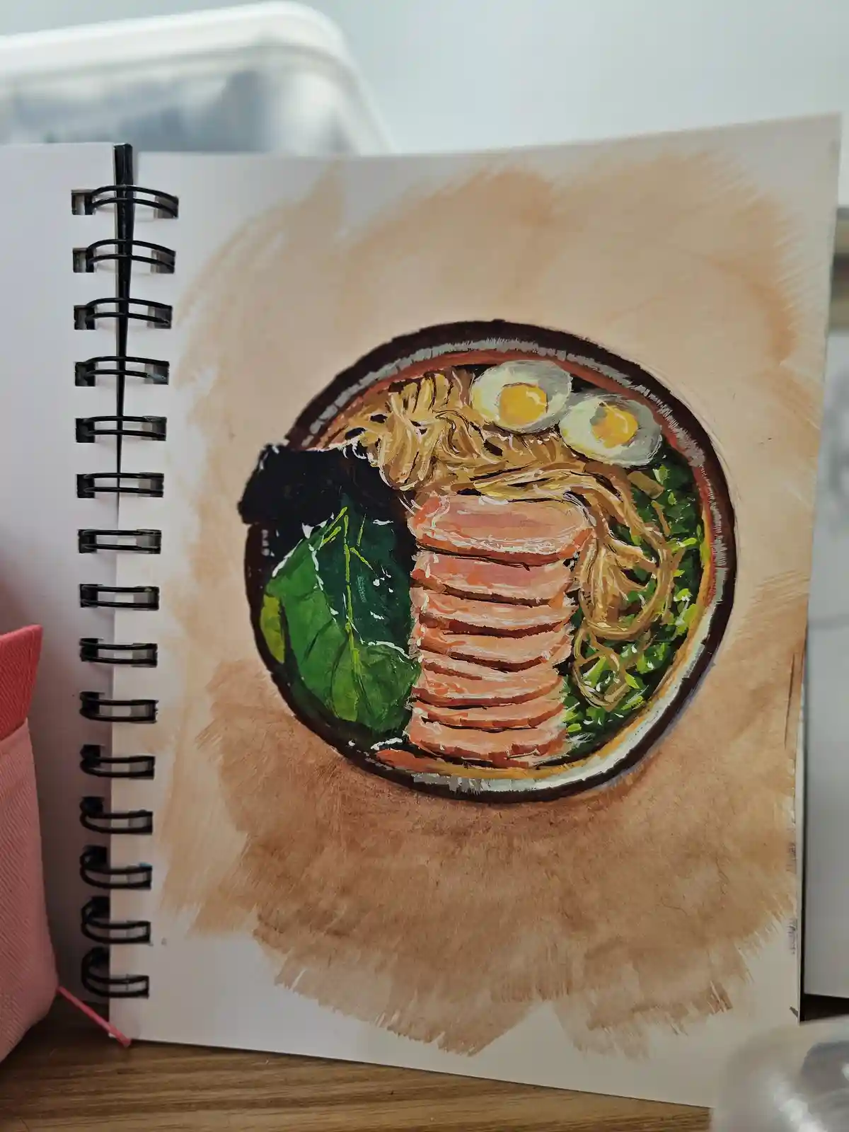 A hand-drawn watercolor illustration in a spiral-bound sketchbook depicts a bowl of ramen with noodles, two soft-boiled…