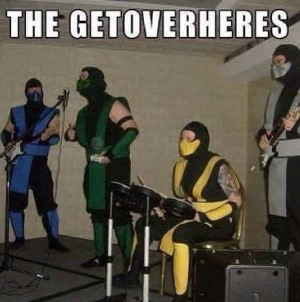 Four people dressed as Mortal Kombat characters — Sub-Zero, Reptile, Scorpion, and a masked guitarist — are performing in a…