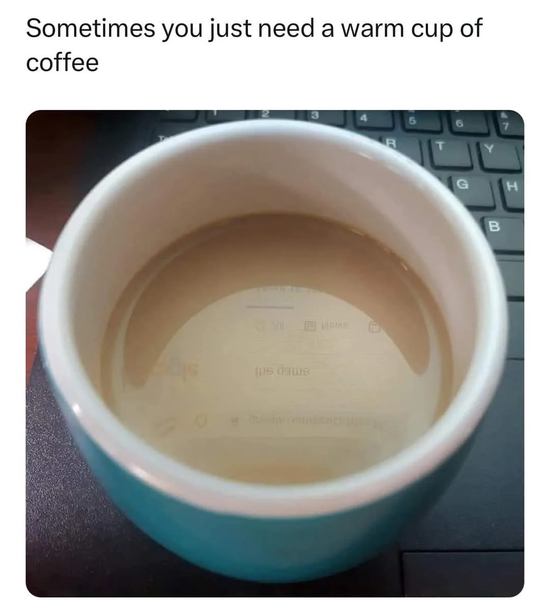 A top-down view of a teal coffee mug with very little coffee left, sitting on a black keyboard. The bottom of the mug…