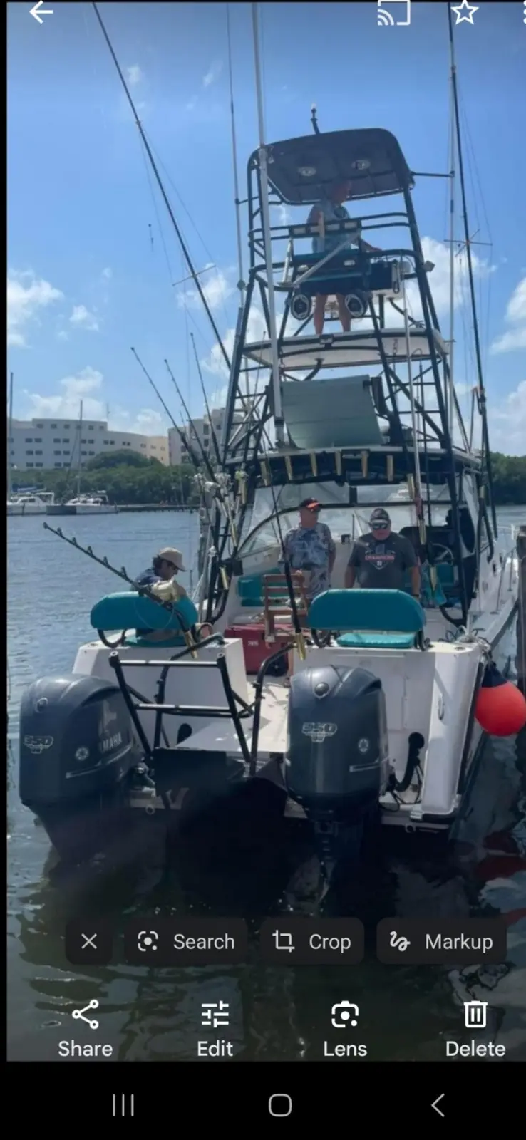 A large, multi-level fishing boat with several men on board is docked in a marina under a sunny sky. The boat has two…