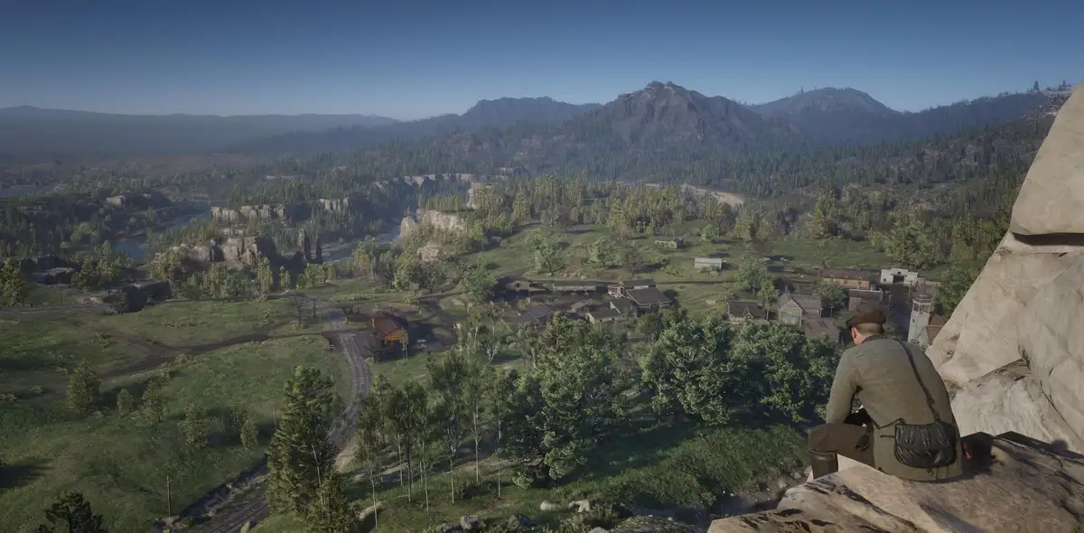 A video game screenshot shows a man in a hat and coat sitting on a rocky cliff overlooking a small, rustic western town…